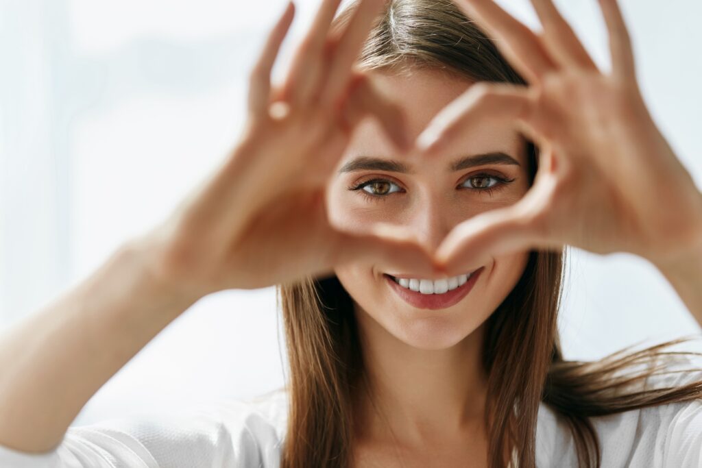 Young woman creating a heart shape with her fingers in front of her face, framing her eyes..