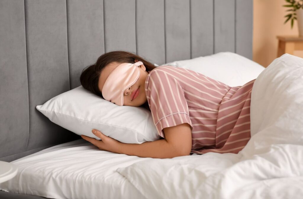 A woman sleeping in bed with a pink eye mask on her eyes.