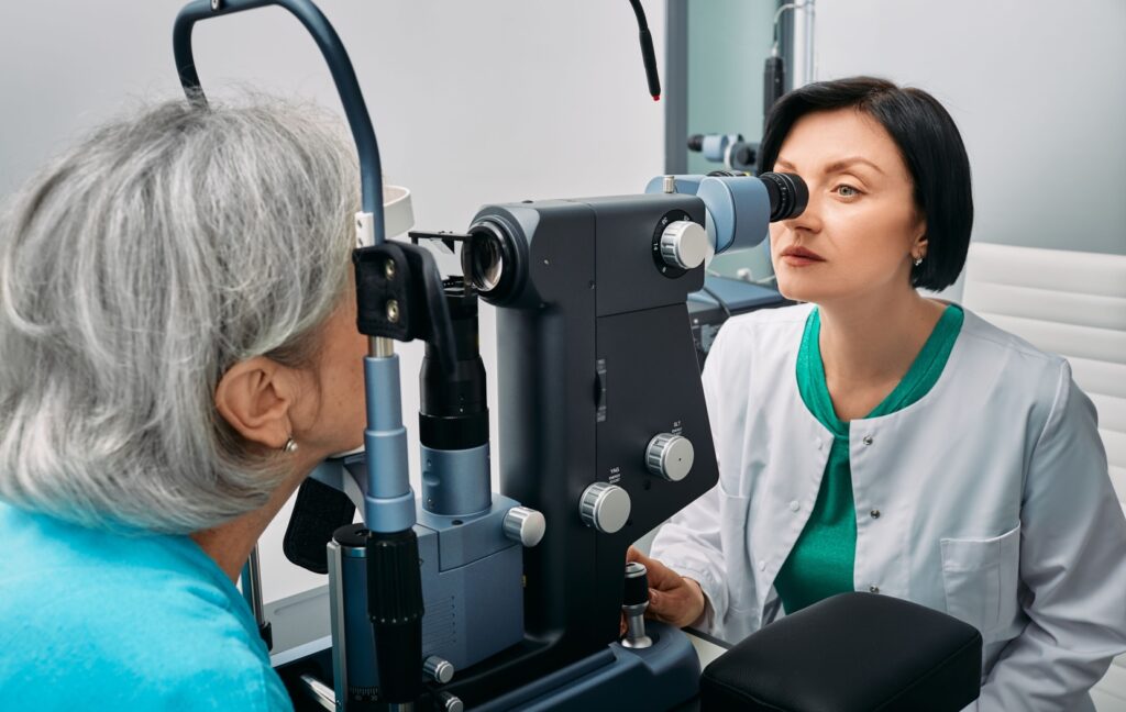 An optometrist uses a slit lamp to examine the back of their senior patient's eye to check for eye diseases.