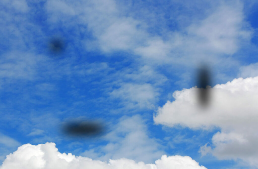 A blue sky with fluffy white clouds is obstructed by a few dark sunspots across the image.